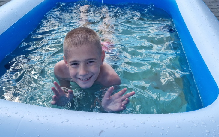 Chłopiec w basenie, uśmiechający się i machający rękami.