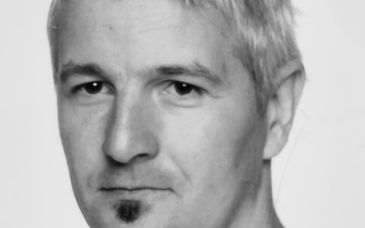 Czarno-biała fotografia mężczyzny z wyrazistym spojrzeniem.