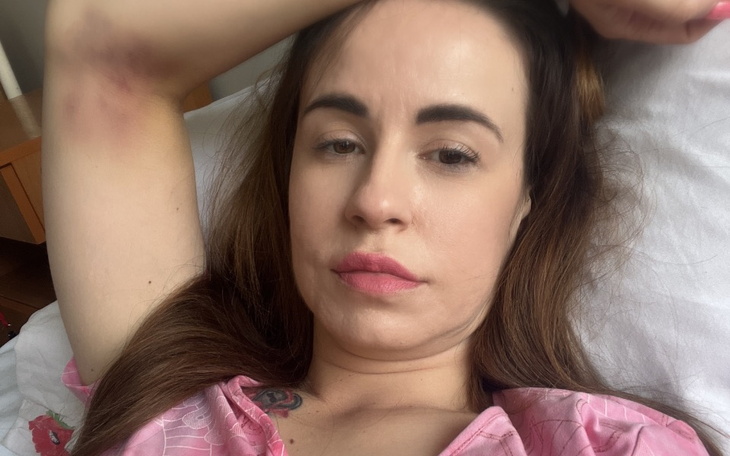 Kobieta leży na łóżku, wygląda na zmęczoną, z lekkim uśmiechem.