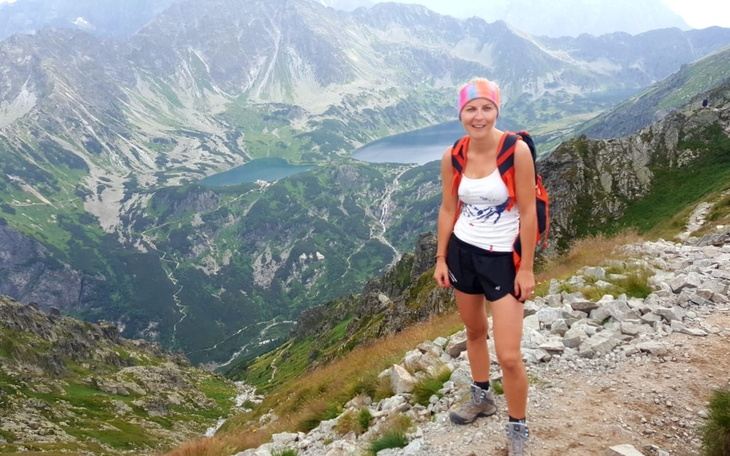 Kobieta w górach, z plecakiem, z widokiem na jezioro.