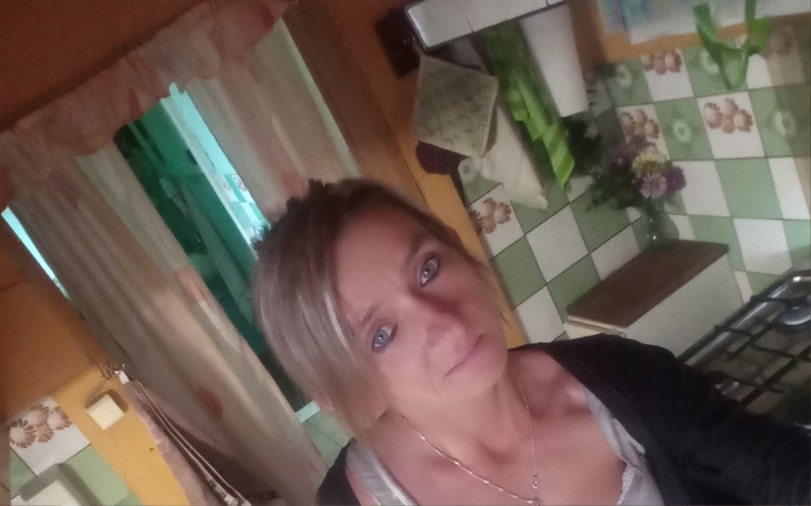 Kobieta w kuchni, uśmiechająca się do aparatu, w tle zielone kafelki.