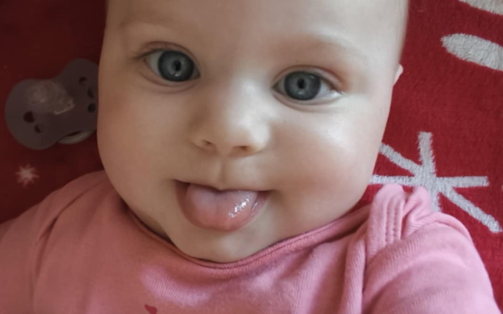 Urocza niemowlęca buzia z niebieskimi oczami i wystawionym językiem.