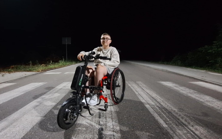 Młody chłopak na wózku inwalidzkim na drodze nocą.