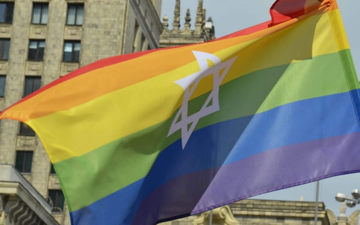 Tęczowa flaga z gwiazdą Dawida na tle budynków.