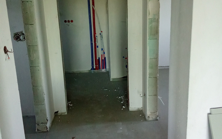 Pusty korytarz w trakcie remontu, widoczne rury i ściany.