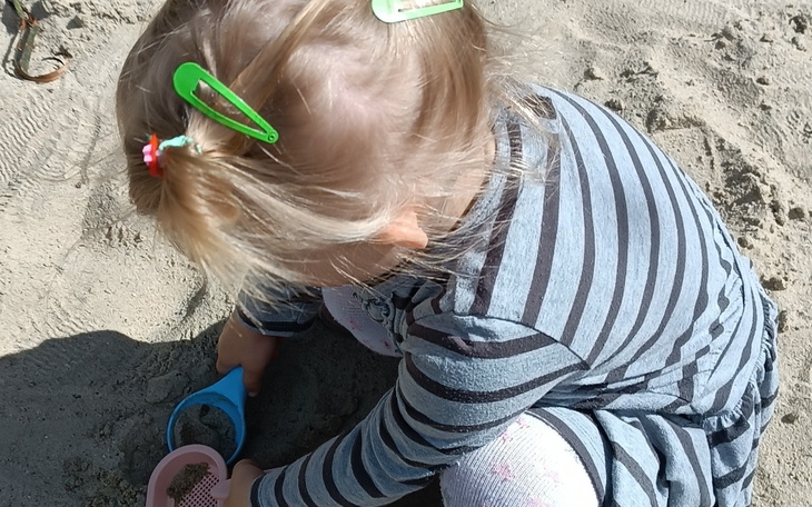 Mała dziewczynka bawi się w piasku, używając łopatki.