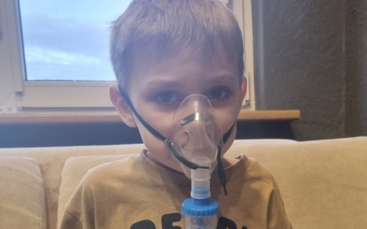 Chłopiec z maską inhalacyjną, wygląda na zmartwionego.