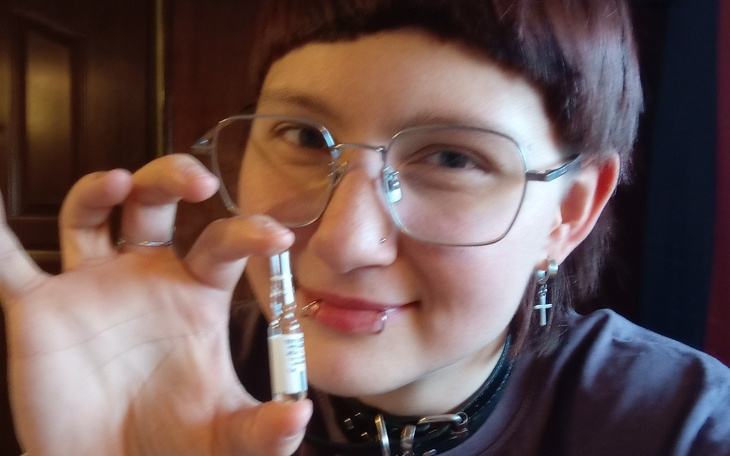 Osoba trzymająca fiolkę z lekiem, uśmiechnięta i z okularami.