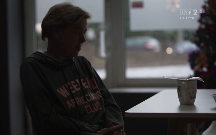 Osoba siedząca przy stole, wpatrzona w pusty kubek.