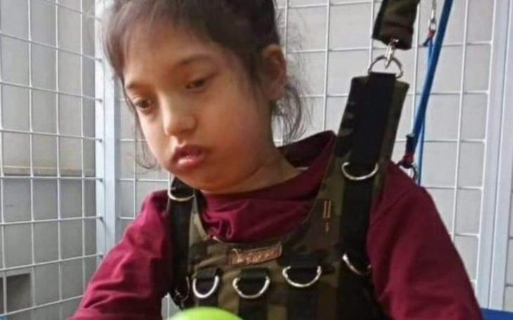 Dziewczynka w uprzęży, skupiona na zabawie z piłką.