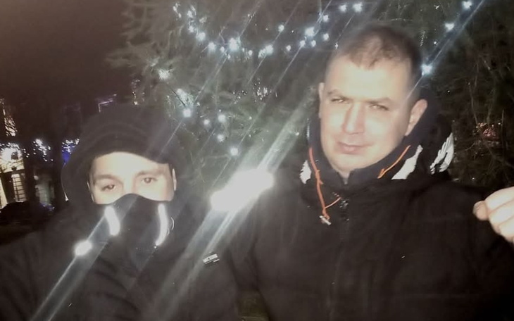 Dwaj mężczyźni pozują w zimowej scenerii, otoczeni świątecznymi światłami.