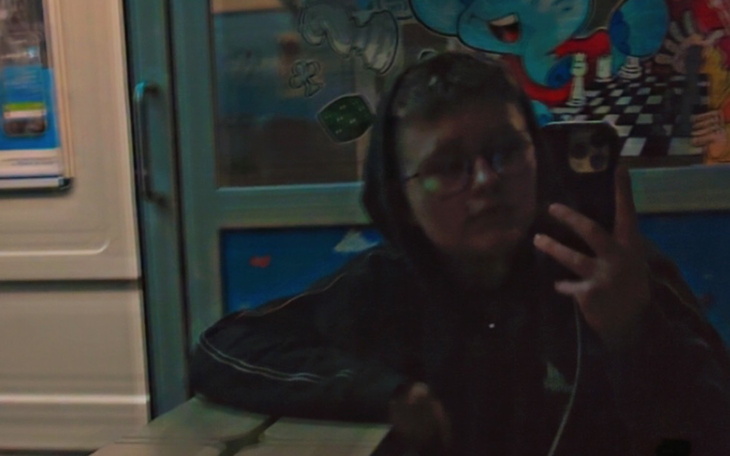 Młoda osoba w bluzie, robiąca selfie w odbiciu szyby.