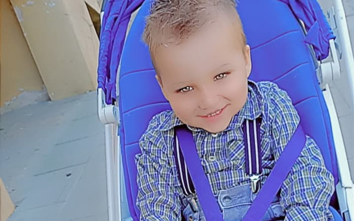 Uśmiechnięty chłopiec w wózku, ubrany w koszulę w kratę.