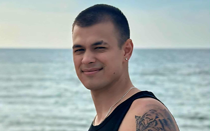 Mężczyzna na plaży z uśmiechem, w tle morze.