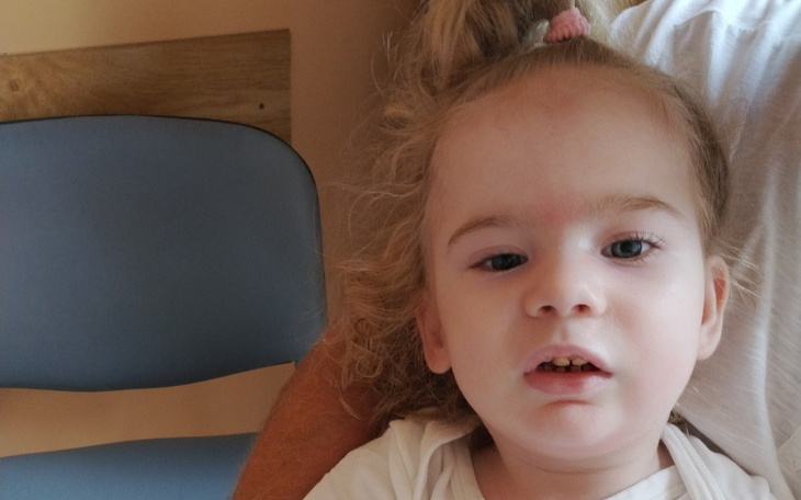 Mała dziewczynka z kręconymi włosami, siedząca na kolanach.