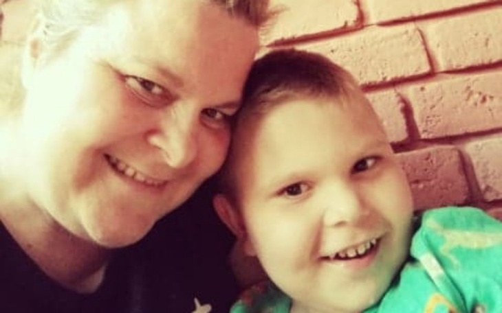 Uśmiechnięta kobieta z dzieckiem na tle ceglanej ściany.