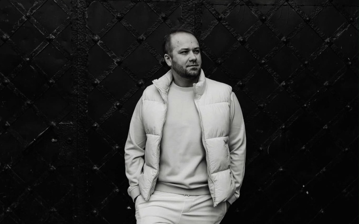 Mężczyzna w białej pikowanej kurtce na czarnym tle, minimalistyczny portret.