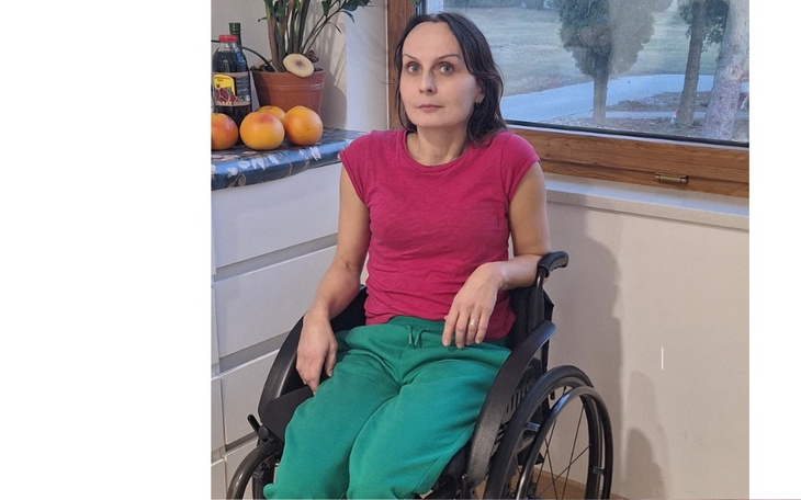 Kobieta na wózku inwalidzkim, siedząca przy oknie w domu.