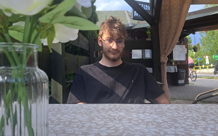 Mężczyzna w okularach, z ręką na głowie, w ciemnym otoczeniu.