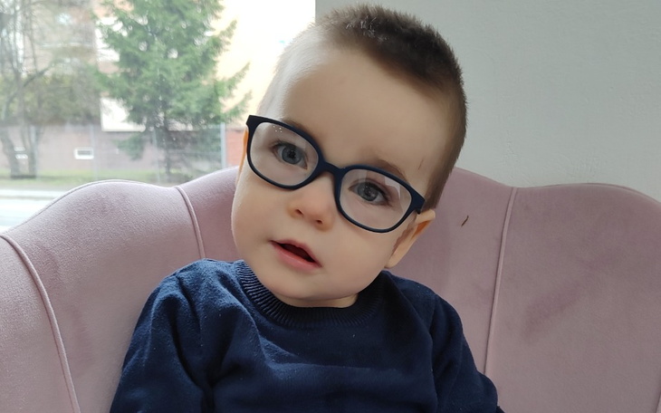 Mały chłopiec w okularach siedzi na różowej kanapie.