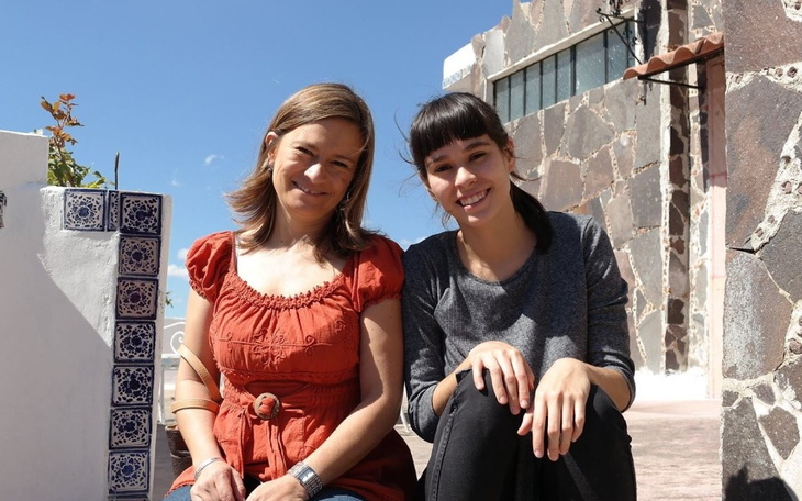 Dwie kobiety uśmiechają się na tle kamiennego budynku.