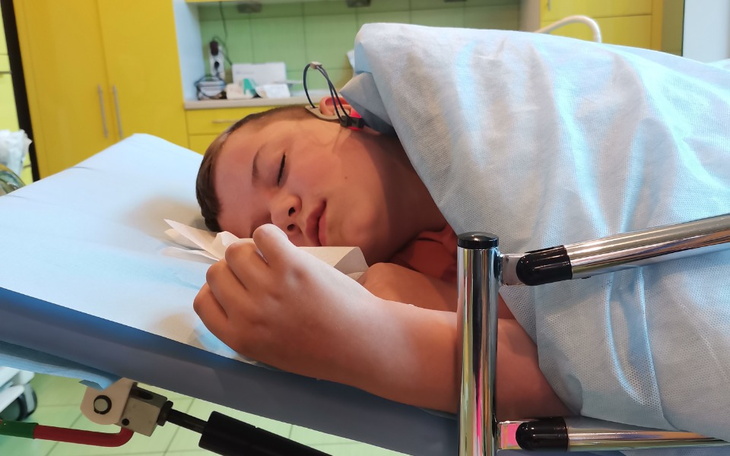 Chłopiec w szpitalu, śpiący na łóżku z opaską na głowie.