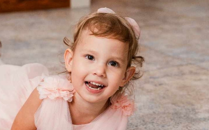 Uśmiechnięta dziewczynka w różowej sukience bawi się na podłodze.