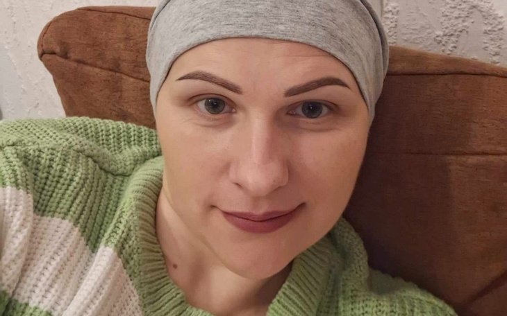 Kobieta w szarej chustce, uśmiechająca się na kanapie.