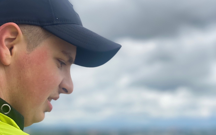 Młody chłopak w czapce, patrzy w dal na tle chmur.