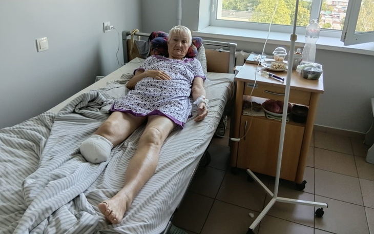 Starsza kobieta leży w łóżku na oddziale szpitalnym, ujęcie z oknem.