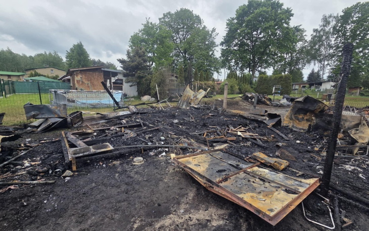 Zniszczona posesja po pożarze, z resztkami budynków i sprzętu.