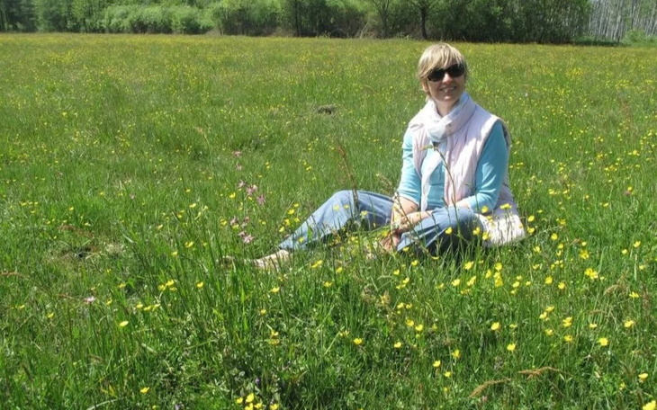 Kobieta siedząca na łące wśród kwiatów, ciesząca się słońcem.