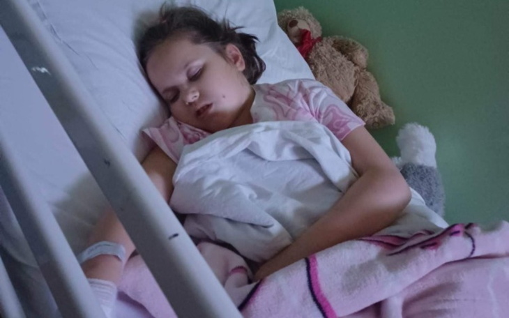 Dziewczynka śpi w szpitalnym łóżku z pluszakami obok.