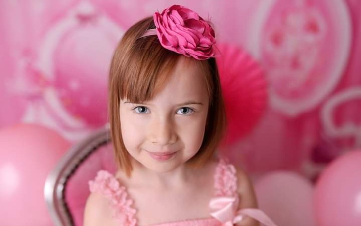 Mała dziewczynka w różowej sukience z kwiatkiem na głowie.