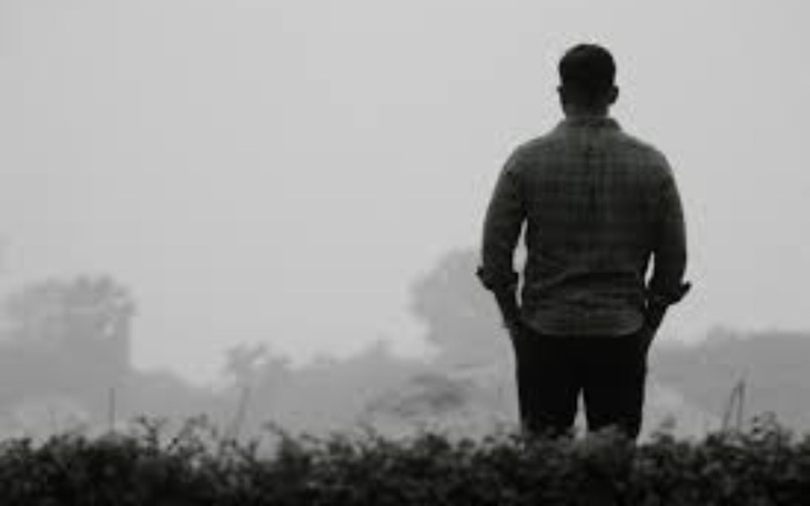 Mężczyzna stojący na tle mglistych drzew, w zamyśleniu.