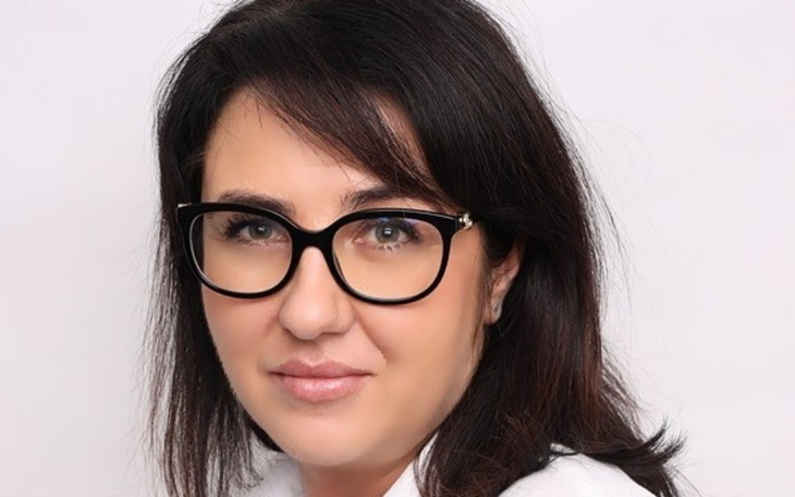 Portret kobiety w okularach, uśmiechającej się do kamery.