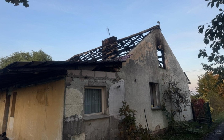 Zniszczony dom z uszkodzeniem dachu, otoczenie zieleni.