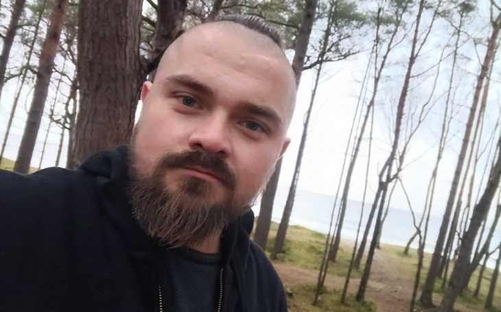 Mężczyzna z brodą w lesie, w tle morze.