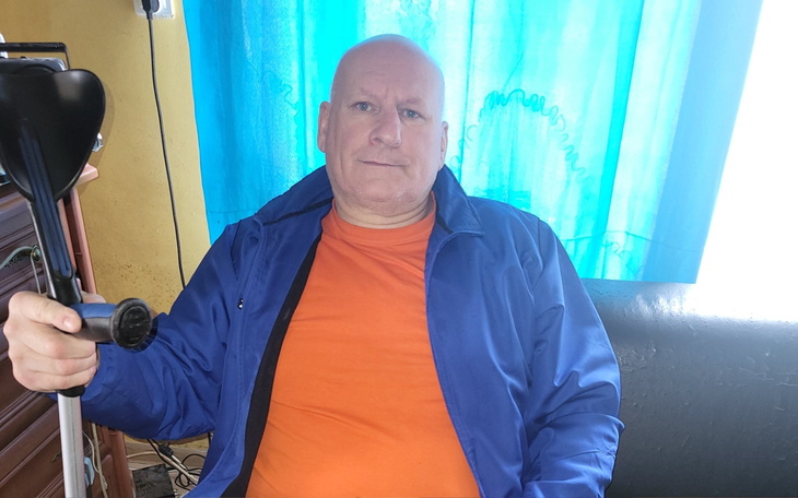 Mężczyzna w niebieskiej kurtce siedzący na kanapie, trzymający laskę.