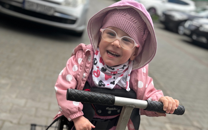 Uśmiechnięta dziewczynka na hulajnodze, ubrana w różowe akcesoria.