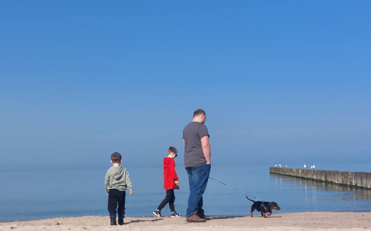 Rodzina spacerująca po plaży z psem w słoneczny dzień.