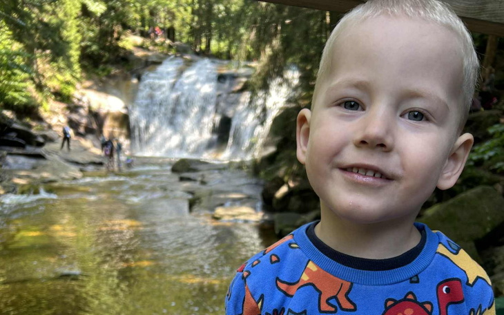 Chłopiec w kolorowej koszulce z dinozaurami przy wodospadzie.