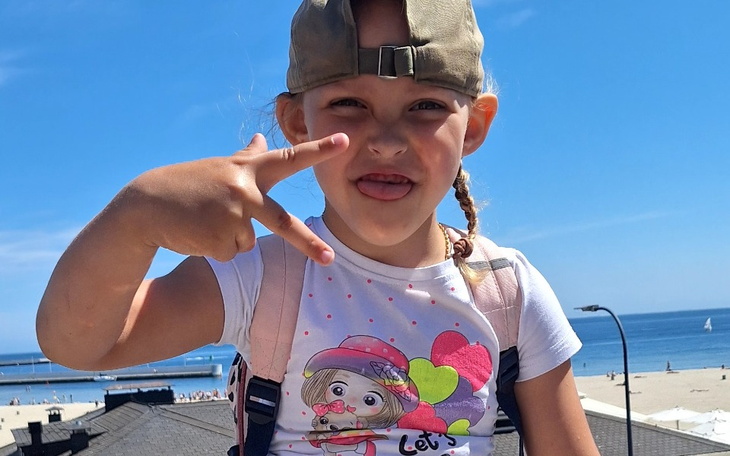 Dziewczynka w czapce, robiąca znak pokoju na tle plaży.