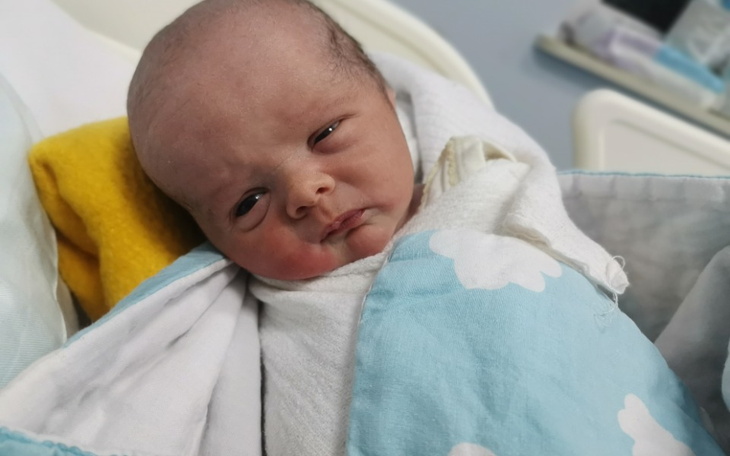 Noworodek owinięty w kocyk, z wyrazem twarzy.