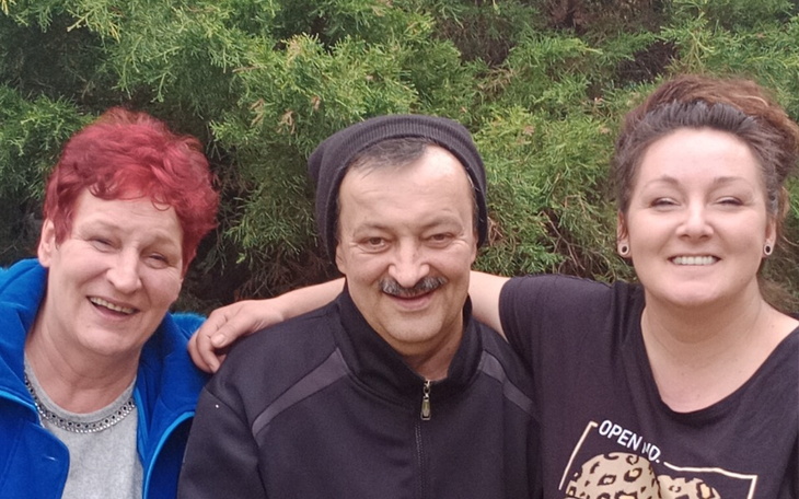 Trzy osoby uśmiechają się na tle zieleni.