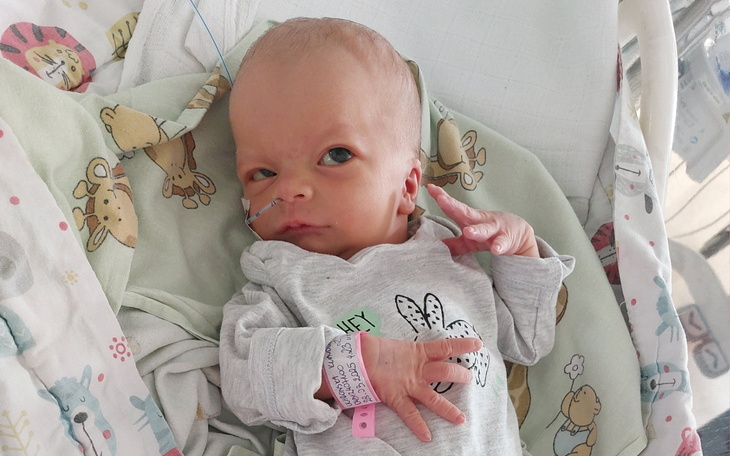 Noworodek w szpitalu, z uśmiechem i opaską na ręce.