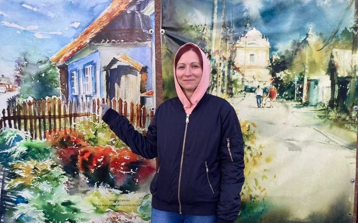 Kobieta wskazująca na malowidło przedstawiające wiejski krajobraz.