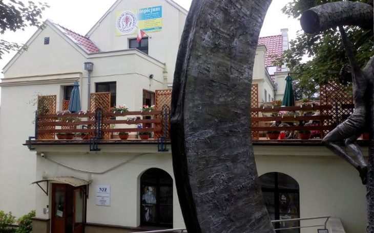 Budynek z tarasem, otoczony zielenią, z rzeźbą w pierwszym planie.