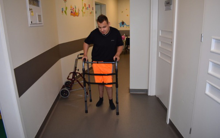 Mężczyzna w pomarańczowych szortach korzystający z chodzika w korytarzu.