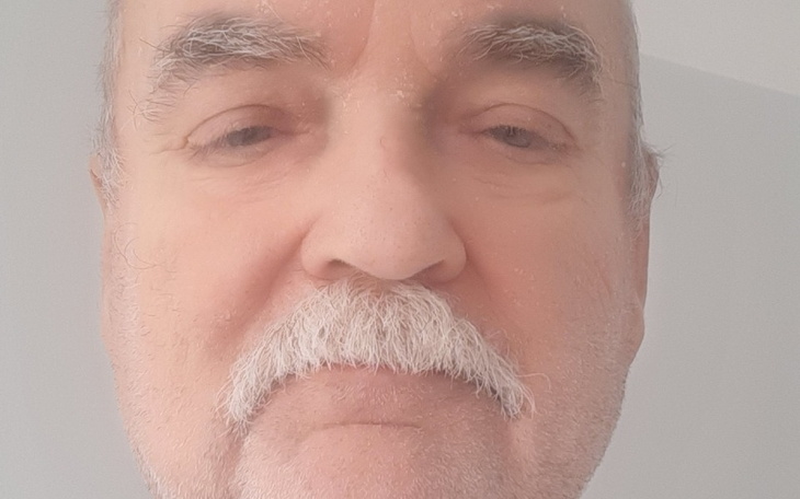 Mężczyzna z siwą brodą i wąsami, patrzący w kamerę.